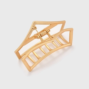 Macro detail of golden metal hair claw clip showing spring mechanism and hollow geometric shape