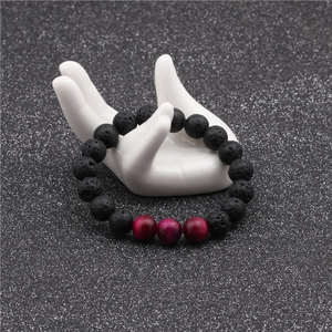 Detailed view of 10mm volcanic lava and tiger eye stone beads on a white ceramic hand