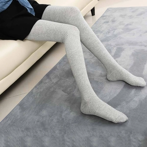 Women long grey knitted over-knee socks in a cozy home setting on a white sofa