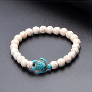 Detail of white turquoise beaded bracelet with a blue turtle charm on black background