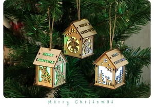 Close-up of wooden LED Christmas houses with elk and Santa hanging on a pine tree