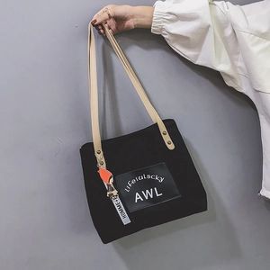 Detail view of black corduroy tote bag with brown leather handles and custom tag