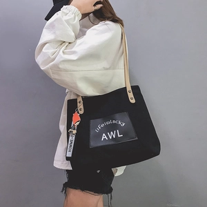 Side view of black canvas tote bag with letter print and cartoon character charm