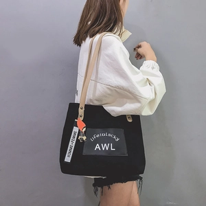 Side view of a black canvas tote bag with beige straps and decorative charms on a model