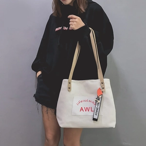 Detail of white canvas tote bag with brown straps and logo print on a model