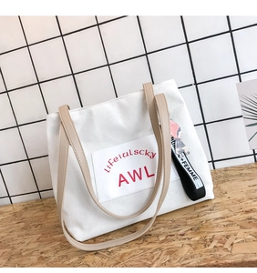 Close-up of white canvas tote bag featuring beige straps and red lettered logo patch