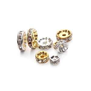 Detailed macro view of gold and silver alloy spacer beads with white rhinestones on white background