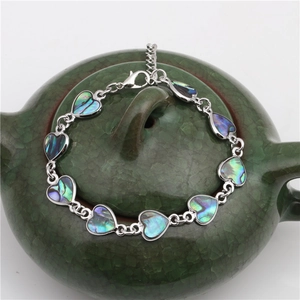 Colorful abalone shell heart link bracelet in silver finish on a ceramic teapot display