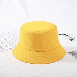 Detail view of yellow cotton bucket hat on white fabric background with lifestyle props