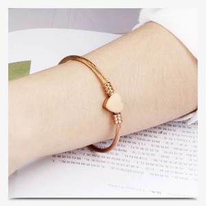 Dettaglio di un bracciale a cavo ritorto dorato con ciondolo a cuore al polso su uno sfondo