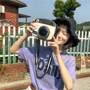 Outdoor shot of a woman holding a stylish camera-shaped crossbody bag in black and beige