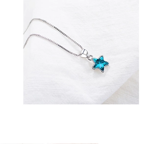 Close-up of blue star crystal pendant with silver box chain on white fabric