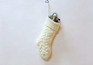 Detailed view of a beige cable-knit Christmas stocking with pine needles and pine cones
