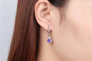 Close-up of elegant silver flower earrings with purple gemstone worn by model