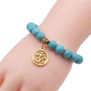 Turquoise bead bracelet with golden Om charm shown on wrist against white background