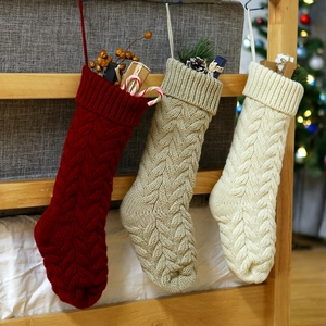 Three cable knit Christmas stockings in red and beige hanging with festive gifts