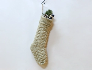 Close-up of beige knitted Christmas stocking with cable pattern and festive pine cones