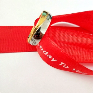 Macro shot of two-tone gold titanium steel couple ring with diamonds on red birthday ribbon