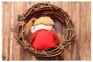 Close-up of a rustic Christmas wreath featuring a faceless gnome and red berries on wood