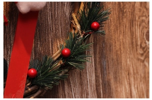Detailed view of Christmas wreath featuring red berries, pine needles and a rustic ribbon