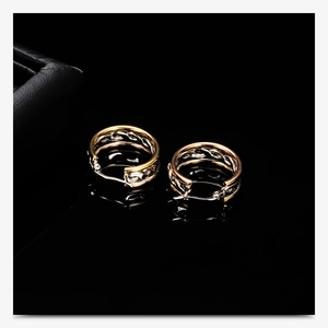 Macro shot of 25mm tri-color gold stainless steel woven hoop earrings on black surface