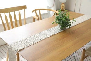 Detailed close-up of handmade beige crochet table runner on a rustic wooden dining table