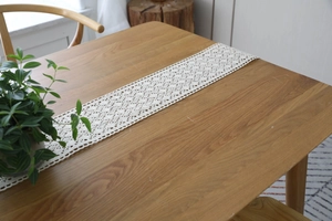 Close-up of beige crochet lace table runner with hollow floral pattern on wood