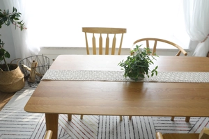 Detail of beige crochet lace table runner on wooden dining table with a green plant