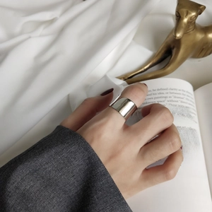 Close-up of a wide polished silver geometric ring worn on a finger over white silk fabric