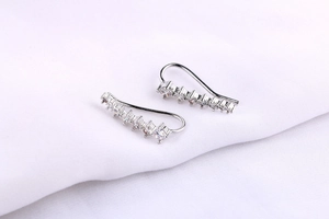 Macro detail of silver ear crawlers with gradient cubic zirconia on white fabric