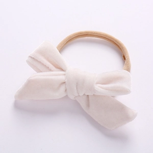 Detail of a handmade beige velvet bow on an elastic nylon headband for infants