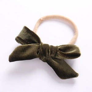 Close-up of a soft green velvet bow headband with a flexible beige nylon strap for babies