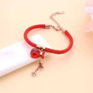 Red braided cord bracelet with rose gold coin charms and a red gourd pendant on a pedestal