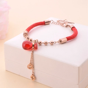 Dettaglio del bracciale a corda rossa con ciondolo a forma di zucca in oro rosa e monete