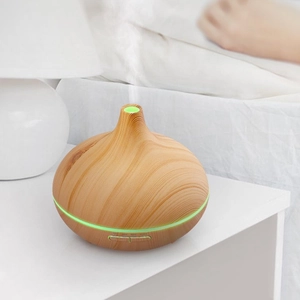 Detail view of wood grain essential oil diffuser with green LED light on a white nightstand
