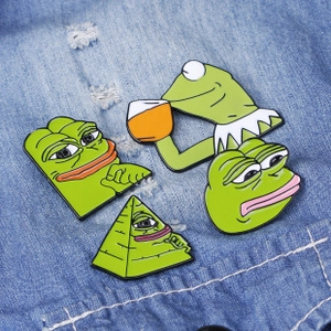 Detail of four green enamel pins with cartoon frog memes on blue denim fabric