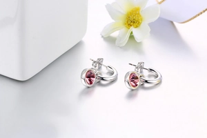 Detail view of silver hoop earrings featuring a round pink crystal on white surface