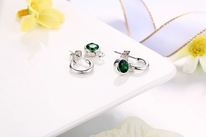 Detailed close-up of silver hoop earrings with round green zircon drop charms