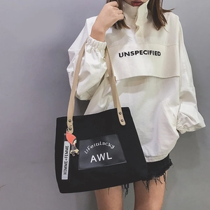 Detail of black canvas tote bag with leather straps and HOMME+FEMME charm accessory