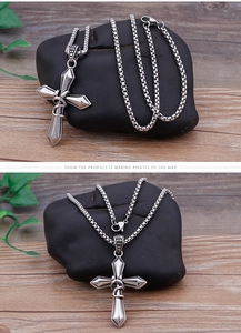 Detailed close-up of a silver cross pendant with a square pearl chain on a wooden base