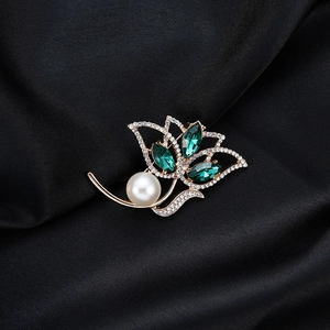 Elegant gold flower brooch with green crystals and pearl on black silk fabric