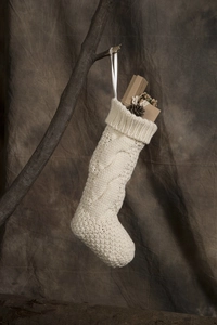 Close-up of cream knit Christmas stocking with cable pattern, pine cone and gift decor