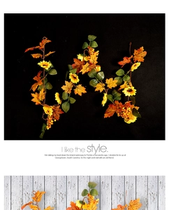Detail of artificial autumn garland with sunflowers, maple leaves, and berries on wood