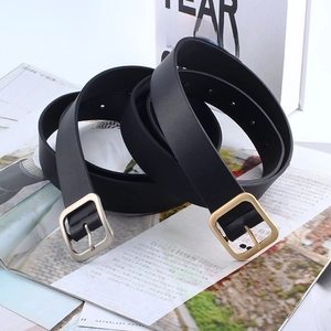 Detail of minimalist black leather belts with square gold and silver pin buckles on books