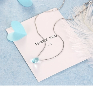 Close-up of a blue teardrop crystal pendant on a silver chain with decorative feathers