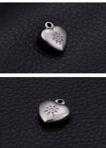 Macro detail of silver stainless steel heart pendant with sun engraving on black leather