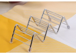 Detail of stainless steel taco holder with wavy compartments and anti-slip feet on a mat