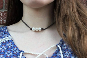 Dettaglio di un girocollo in pelle scura con tre perle bianche naturali da donna