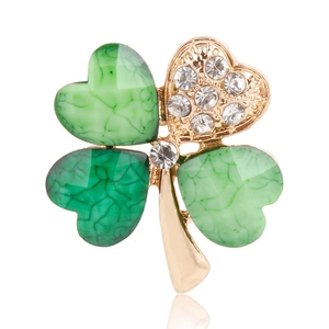 Macro view of gold-plated four-leaf clover brooch with green resin and crystal inlay