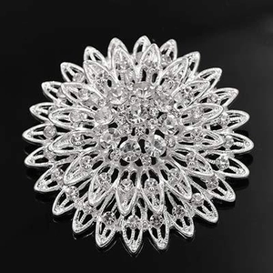 Detail of silver sunflower brooch with shimmering rhinestones on black mirror background